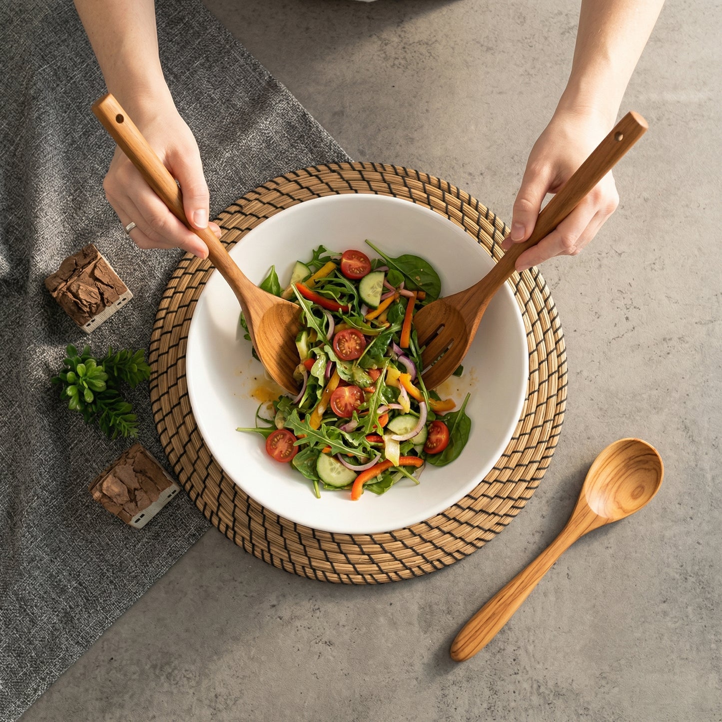 A pair of long-handled golden teak wood salad servers resting on a woven mat, showcasing natural wood grain.