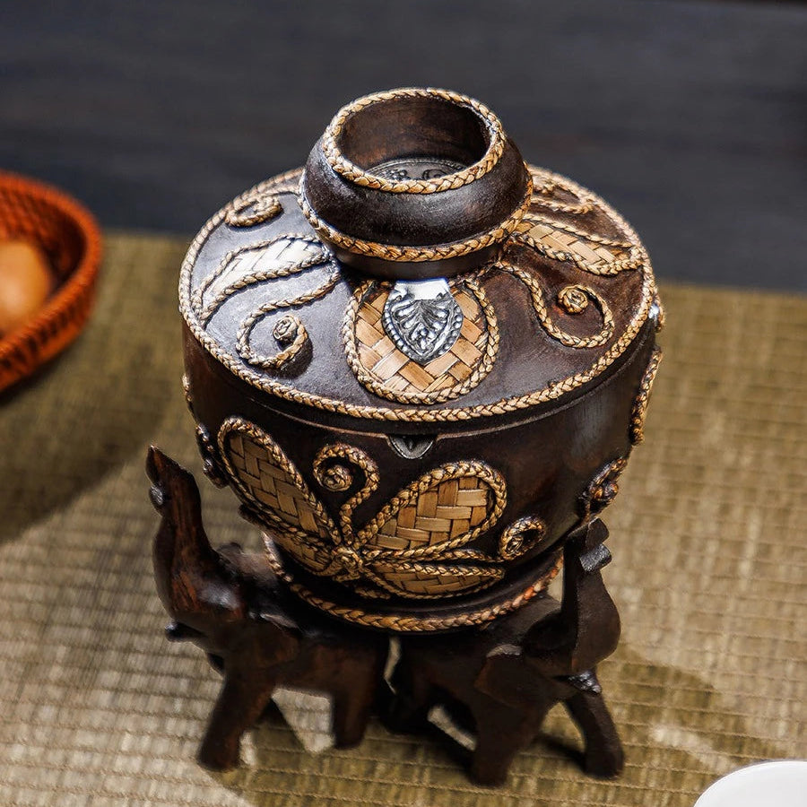 Vintage wooden ashtray with lid resting on three hand-carved elephant pillars, holding a cigarette.