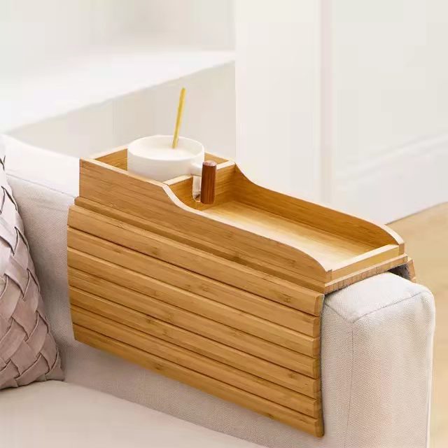 Bamboo sofa tray table with a cup holder and phone slot resting on a couch armrest.