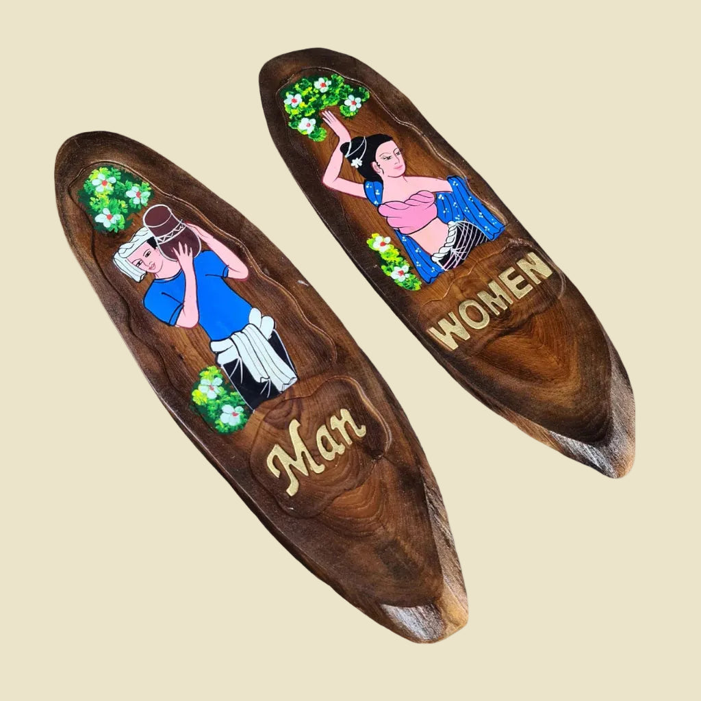A pair of hand-carved teak wood restroom signs featuring traditional Thai man and woman figures.