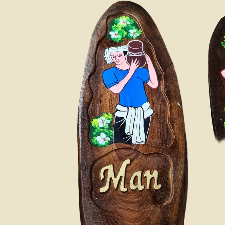 A pair of hand-carved teak wood restroom signs featuring traditional Thai man and woman figures.