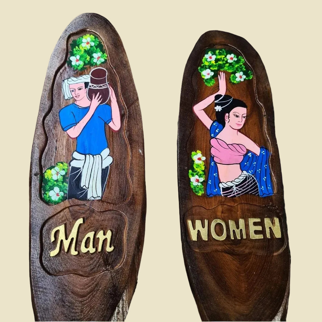 A pair of hand-carved teak wood restroom signs featuring traditional Thai man and woman figures.