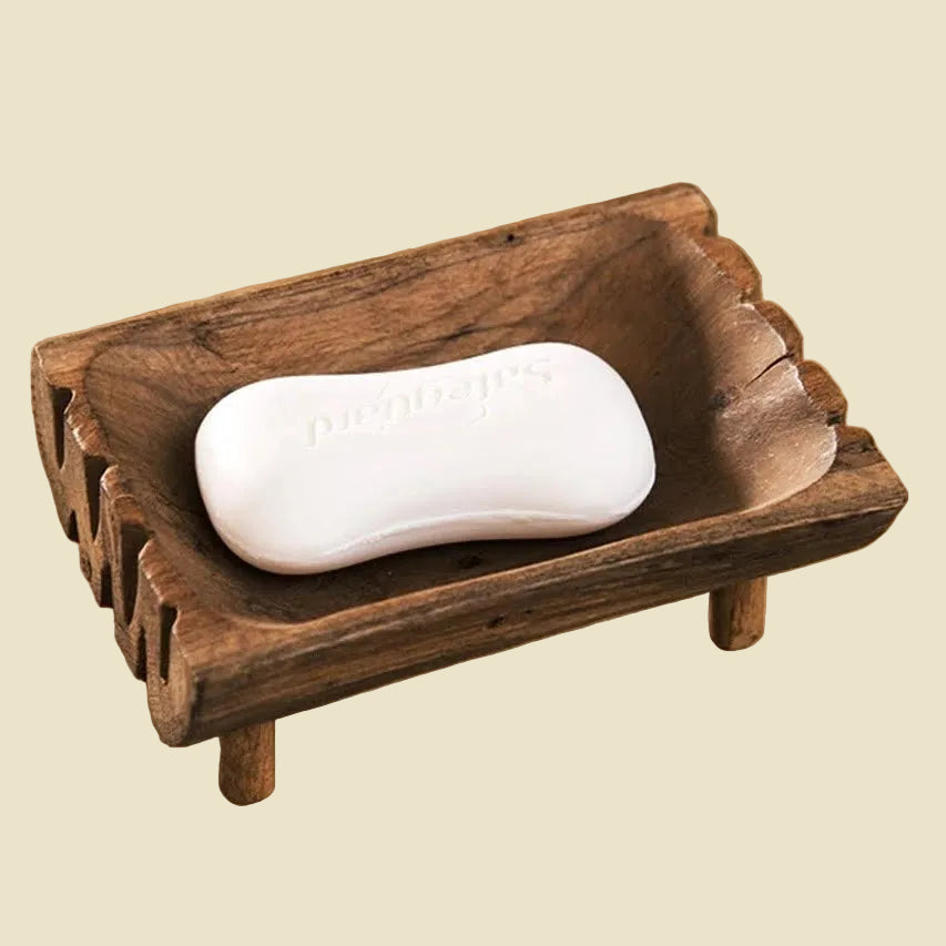 Hand-carved teak wood soap dish with raised legs for drainage, featuring natural wood grain and a rustic artisan design.