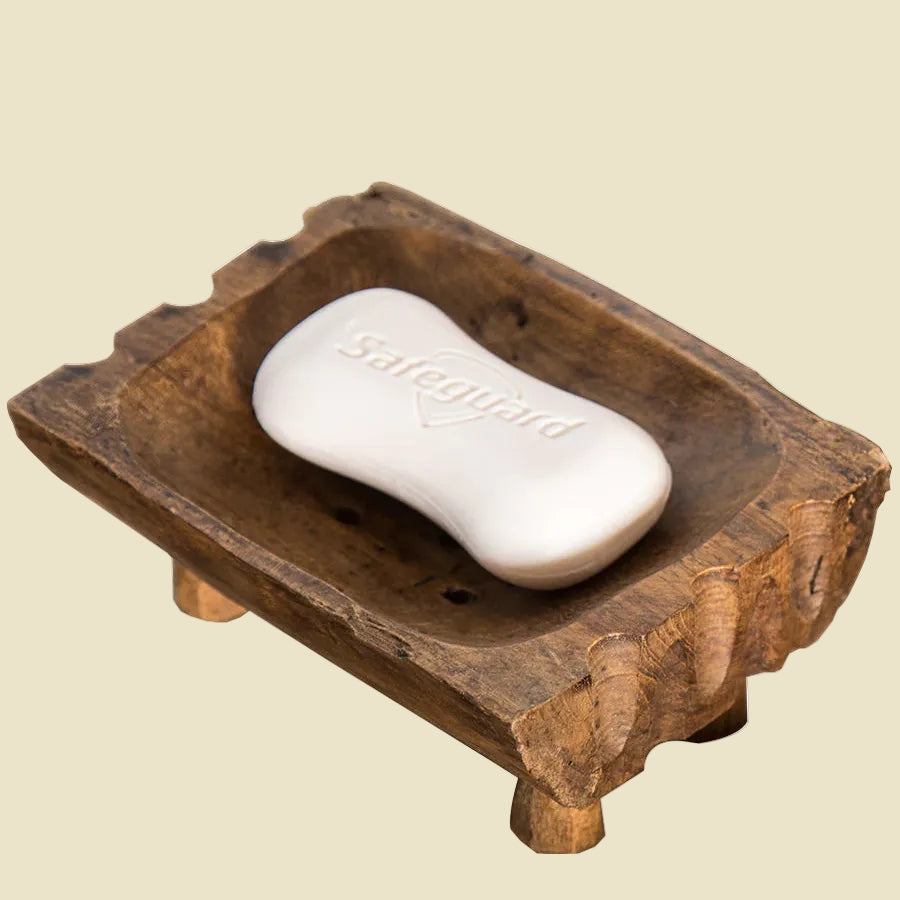 Hand-carved teak wood soap dish with raised legs for drainage, featuring natural wood grain and a rustic artisan design.