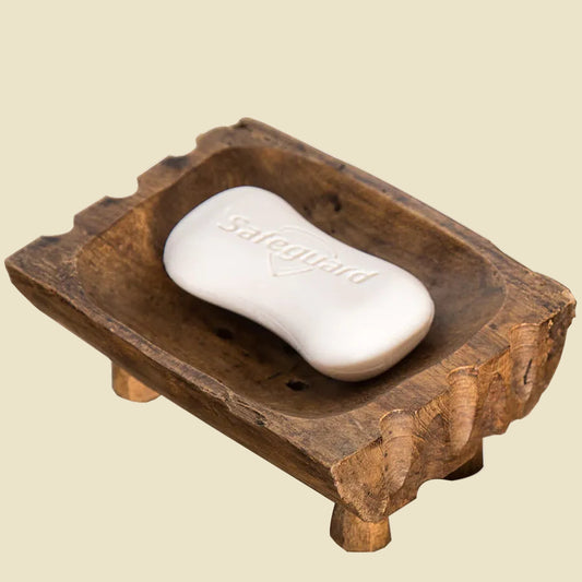 Hand-carved teak wood soap dish with raised legs for drainage, featuring natural wood grain and a rustic artisan design.