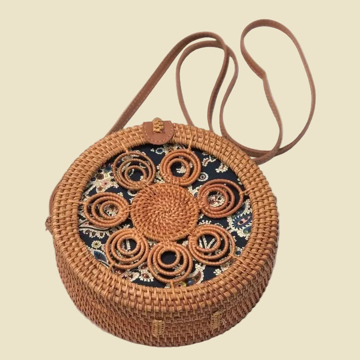 Handmade round rattan crossbody bag with floral woven pattern and leather-style strap, featuring batik fabric lining inside.