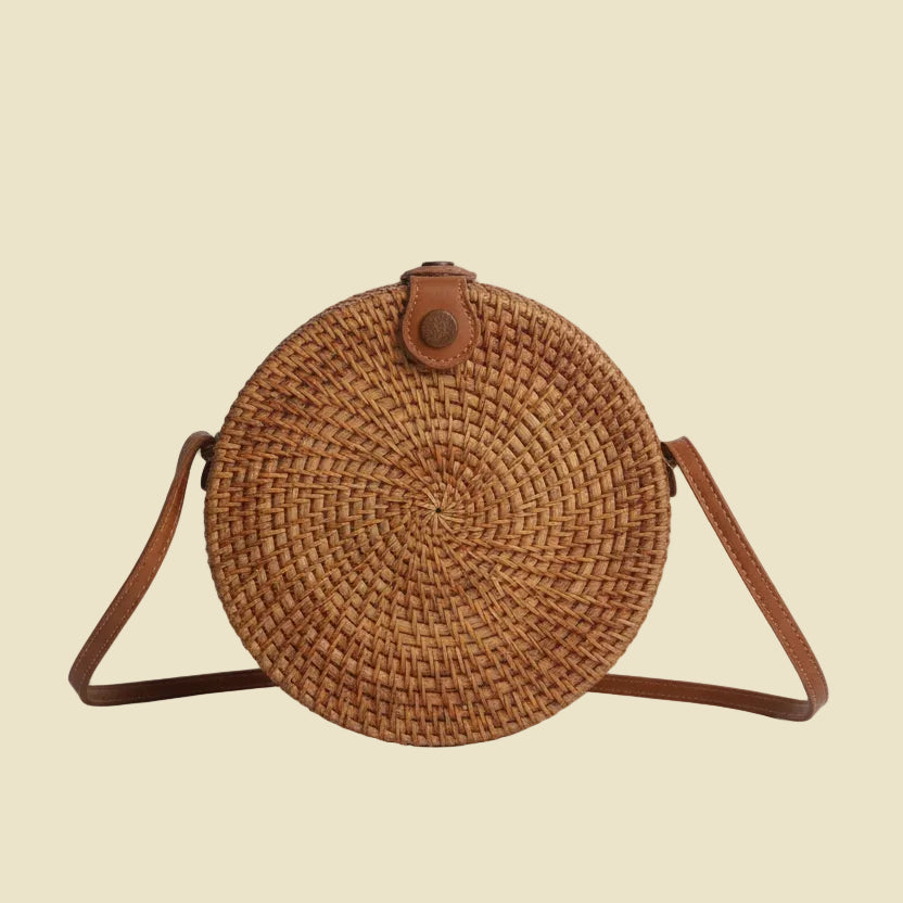 Handmade round rattan crossbody bag with floral woven pattern and leather-style strap, featuring batik fabric lining inside.