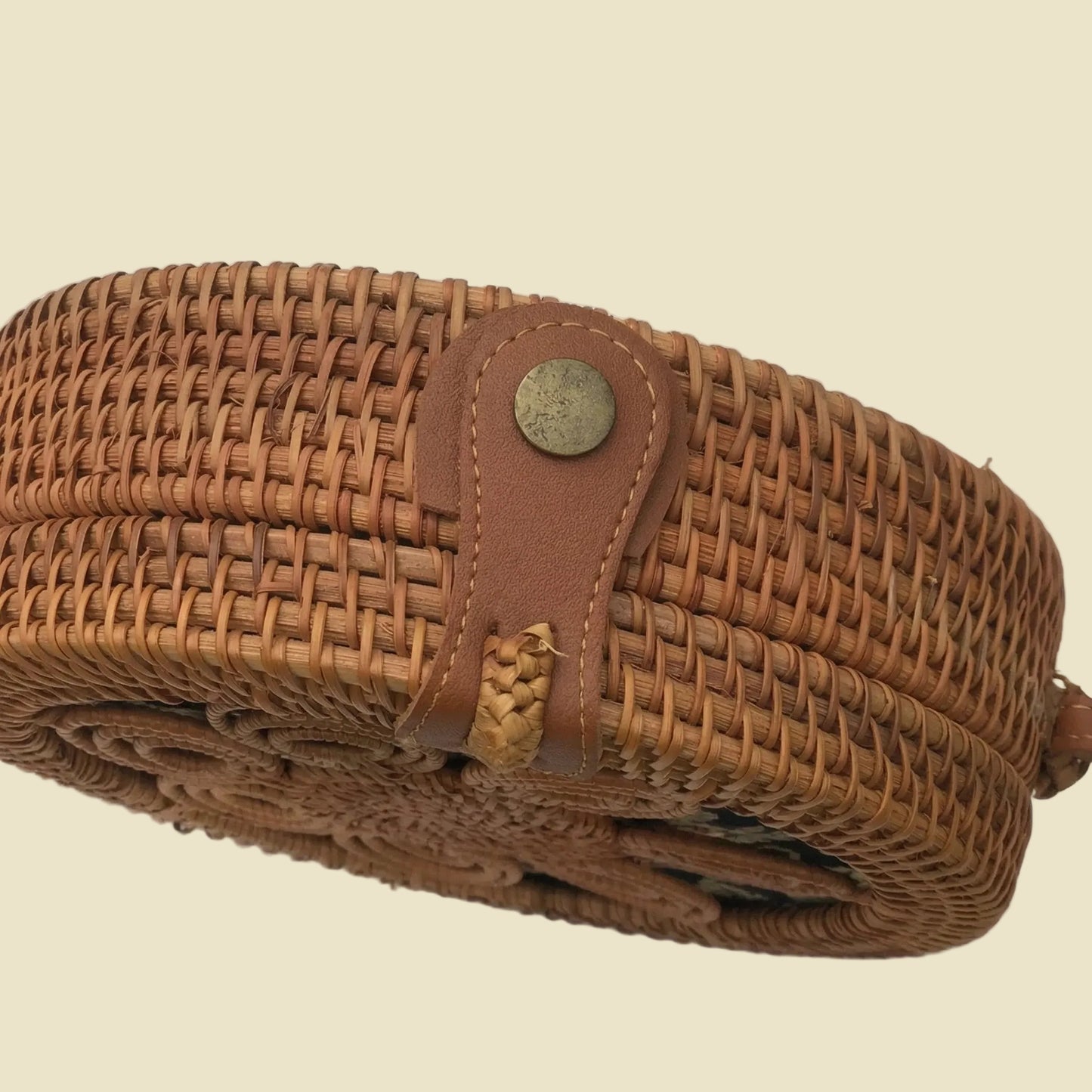 Handmade round rattan crossbody bag with floral woven pattern and leather-style strap, featuring batik fabric lining inside.