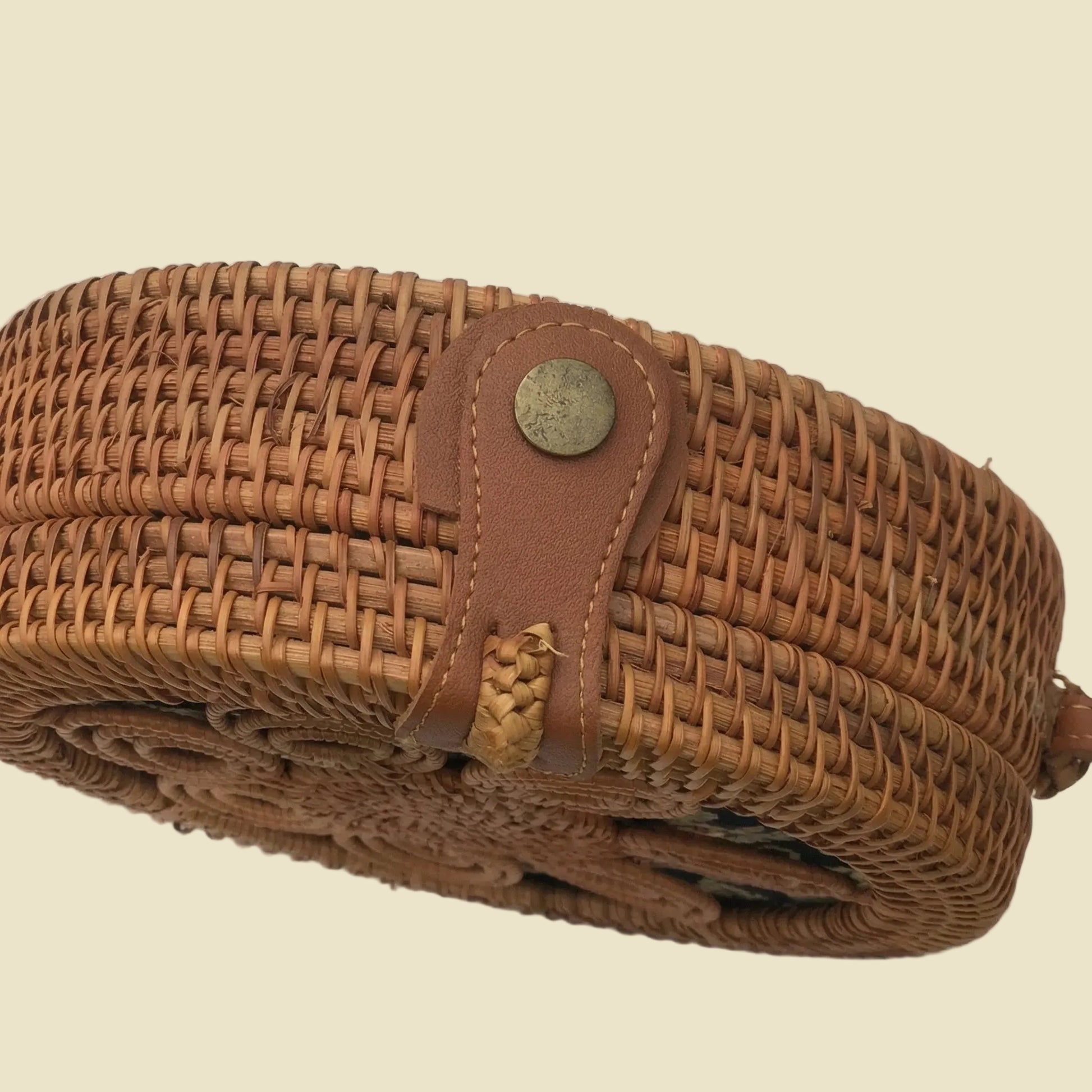Handmade round rattan crossbody bag with floral woven pattern and leather-style strap, featuring batik fabric lining inside.