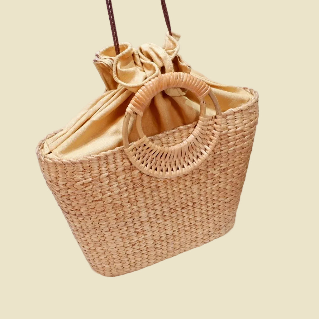Handmade woven water hyacinth tote bag with circular rattan handles and fabric lining, eco-friendly straw bag for summer fashion.