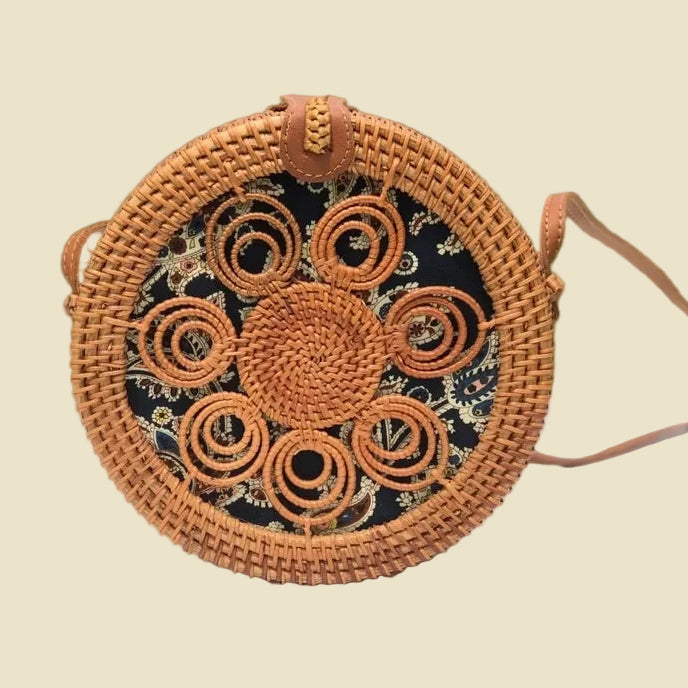 Handmade round rattan crossbody bag with floral woven pattern and leather-style strap, featuring batik fabric lining inside.