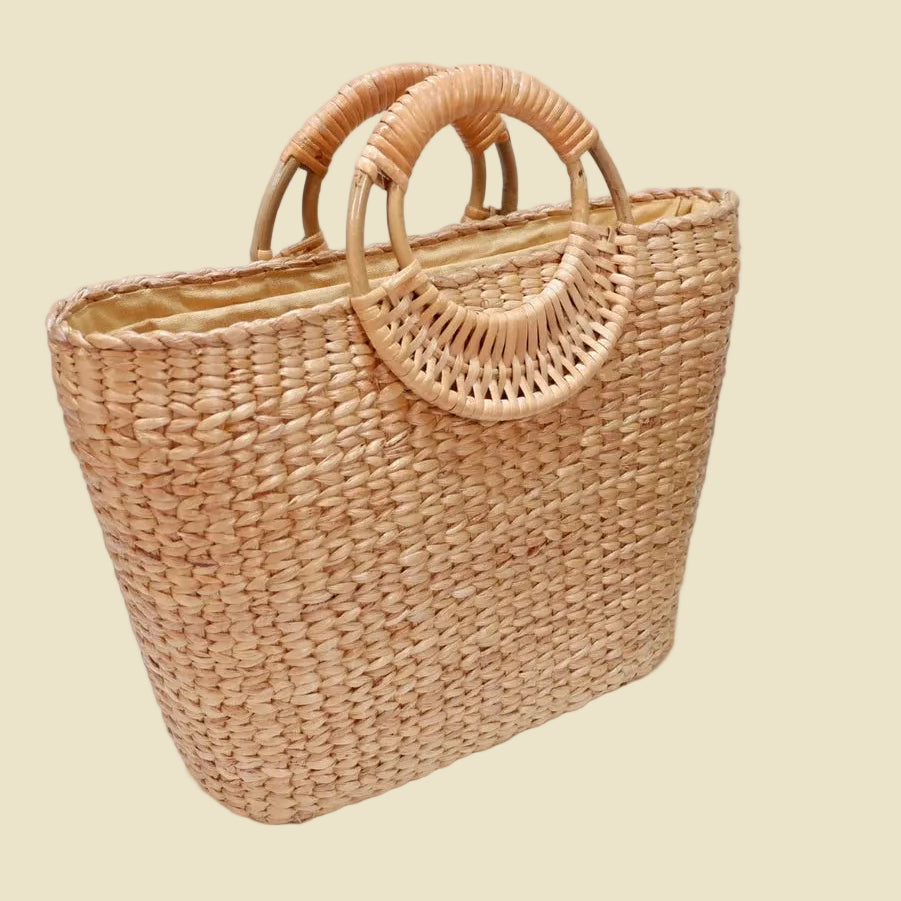Handmade woven water hyacinth tote bag with circular rattan handles and fabric lining, eco-friendly straw bag for summer fashion.