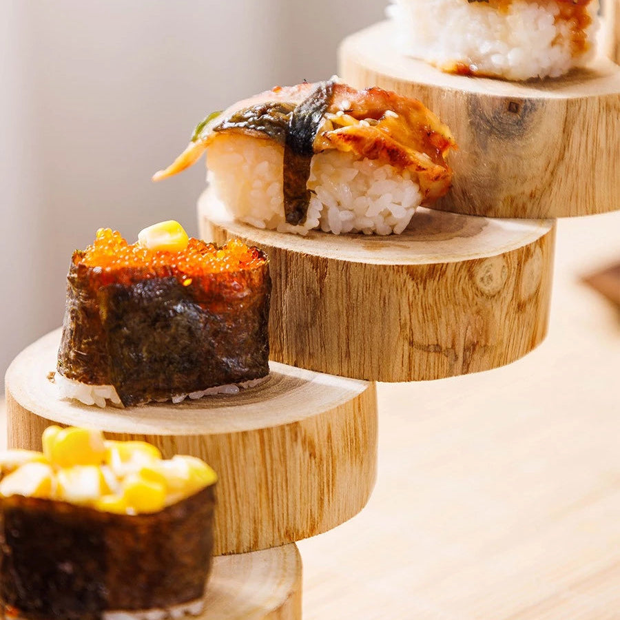 Rustic rotating wooden sushi stand displaying sushi rolls on a multi-tiered staircase design with chopsticks in the holder.