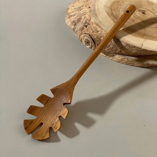 Solid grade-A teak wood pasta server and spaghetti spoon resting on a kitchen counter.