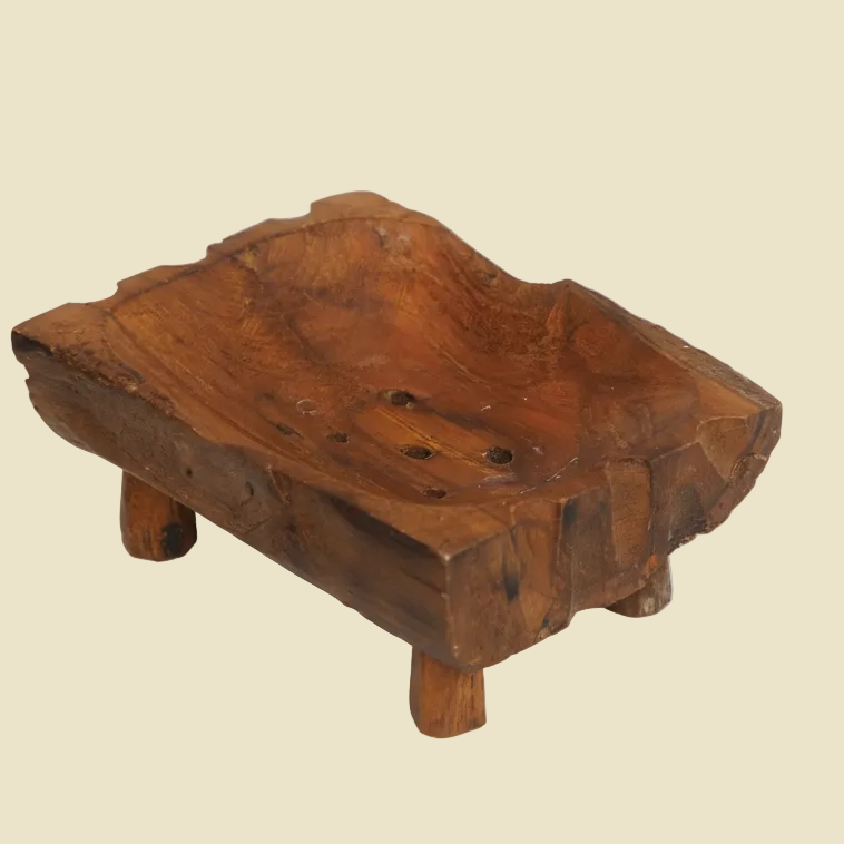 Hand-carved teak wood soap dish with raised legs for drainage, featuring natural wood grain and a rustic artisan design.