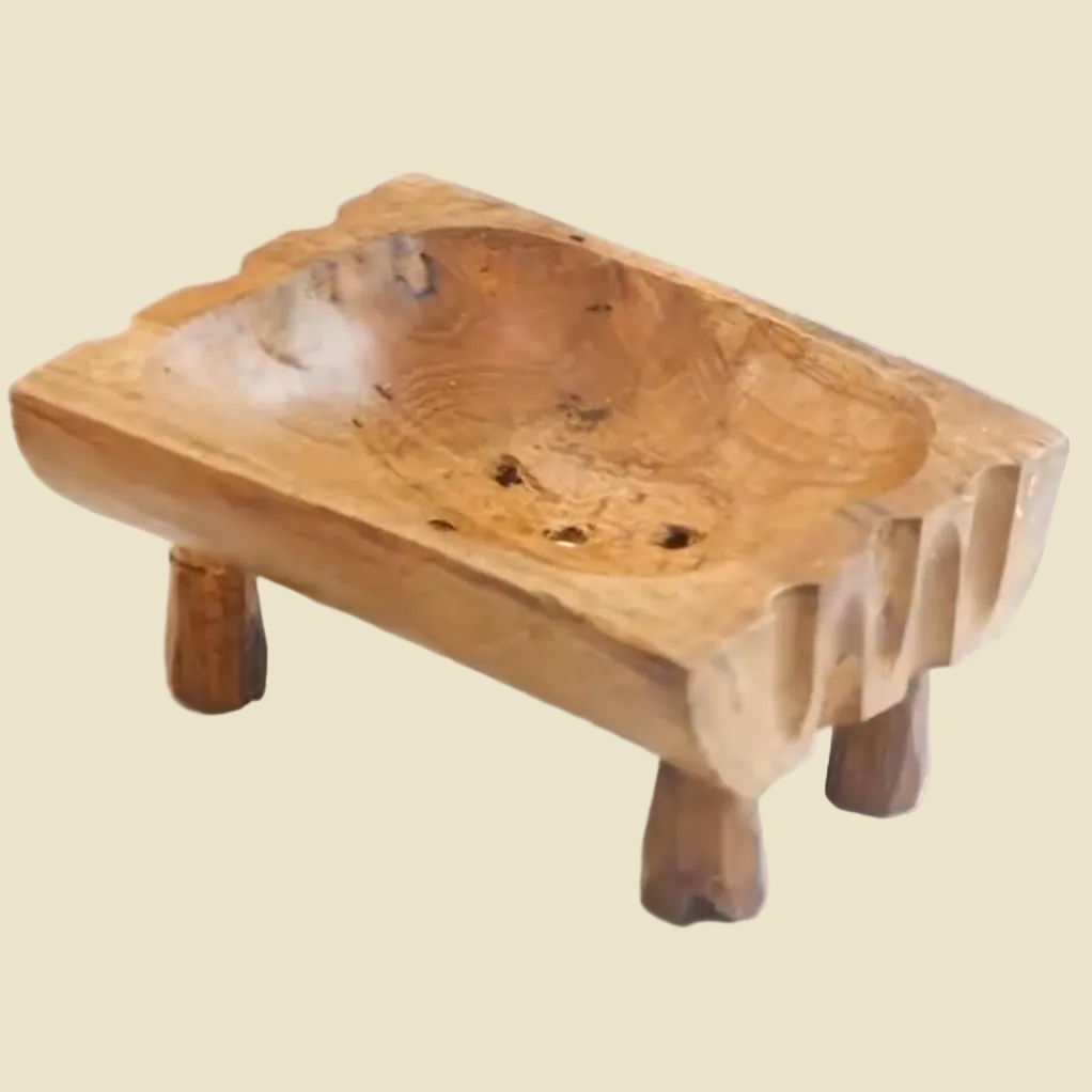 Hand-carved teak wood soap dish with raised legs for drainage, featuring natural wood grain and a rustic artisan design.