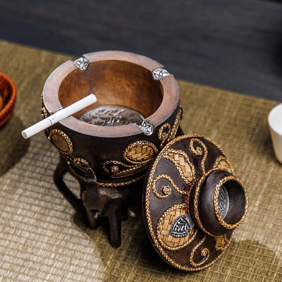 Vintage wooden ashtray with lid resting on three hand-carved elephant pillars, holding a cigarette.