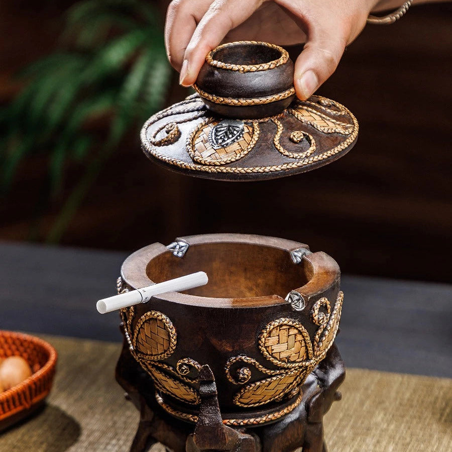 Vintage wooden ashtray with lid resting on three hand-carved elephant pillars, holding a cigarette.
