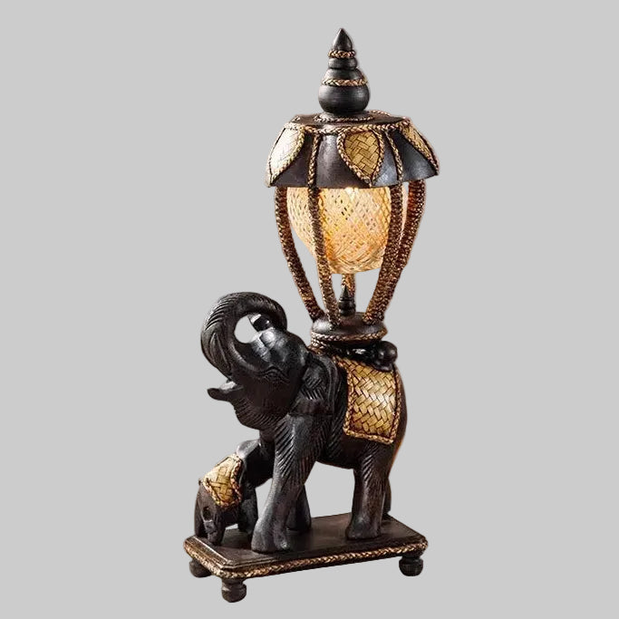 Handcrafted wooden elephant table lamp with a woven bamboo shade lighting up a rustic living space.