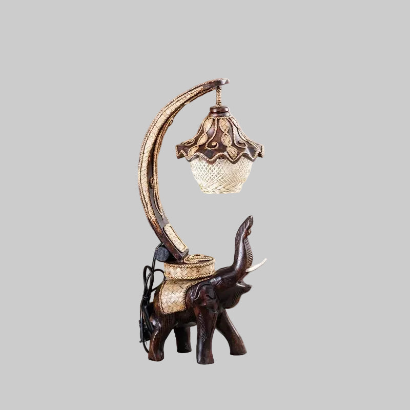 Handcrafted wooden elephant table lamp with a woven bamboo shade lighting up a rustic living space.