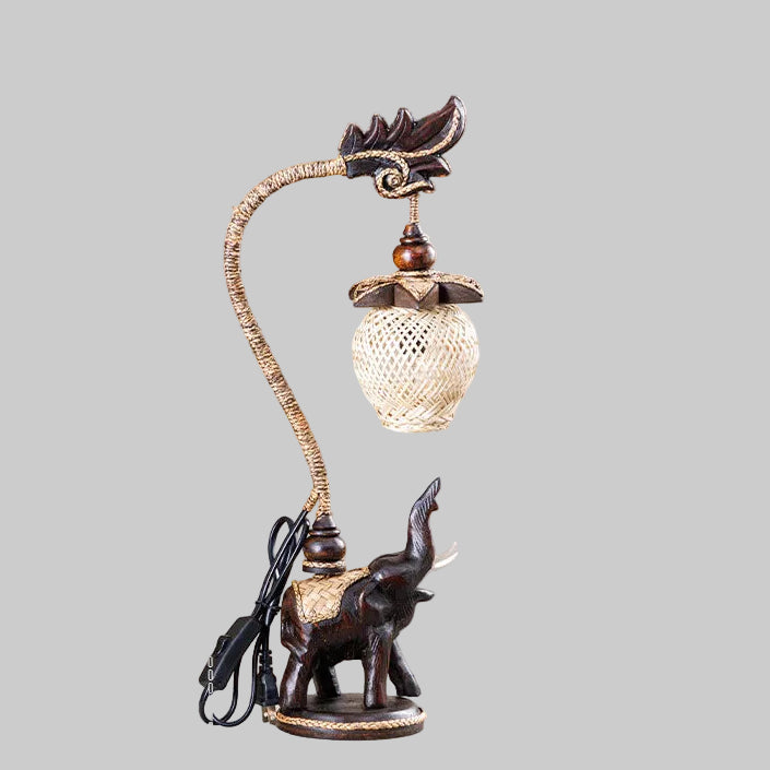 Handcrafted wooden elephant table lamp with a woven bamboo shade lighting up a rustic living space.