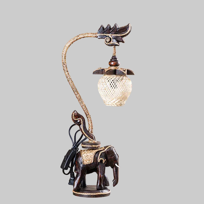 Handcrafted wooden elephant table lamp with a woven bamboo shade lighting up a rustic living space.