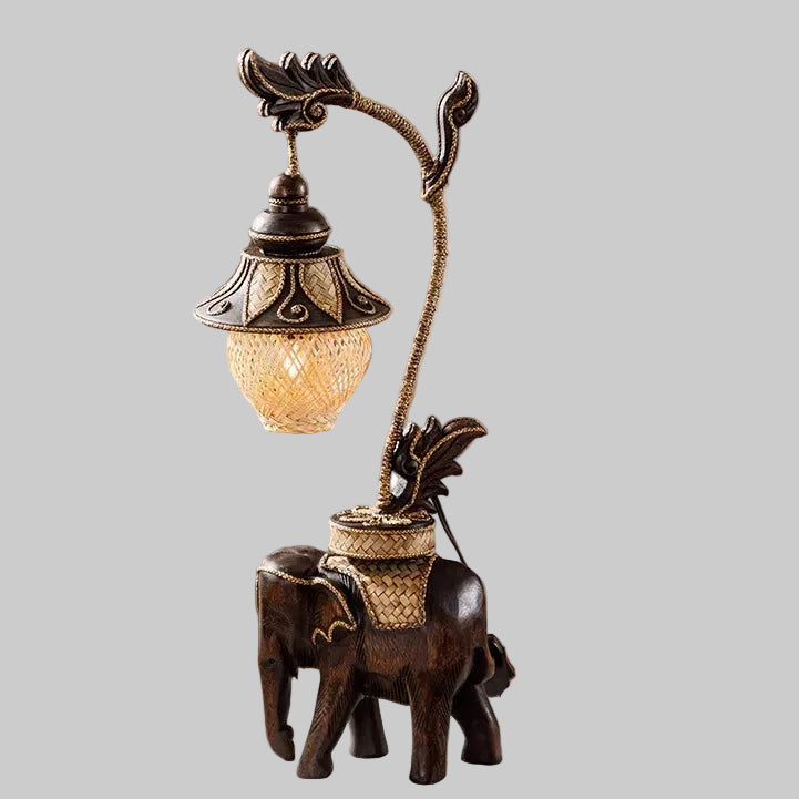 Handcrafted wooden elephant table lamp with a woven bamboo shade lighting up a rustic living space.