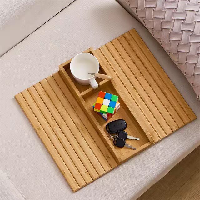 Bamboo sofa tray table with a cup holder and phone slot resting on a couch armrest.
