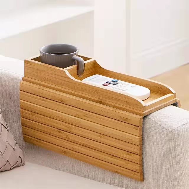Bamboo sofa tray table with a cup holder and phone slot resting on a couch armrest.